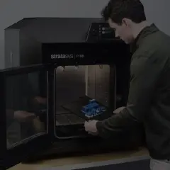 Mężczyzna wkłada wydrukowany model do drukarki 3D Stratasys F120.