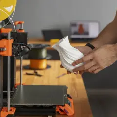 Osoba trzyma biały, wydrukowany w 3D wazon obok drukarki 3D.
