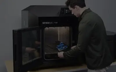 Mężczyzna wkłada wydrukowany model do drukarki 3D Stratasys F120.