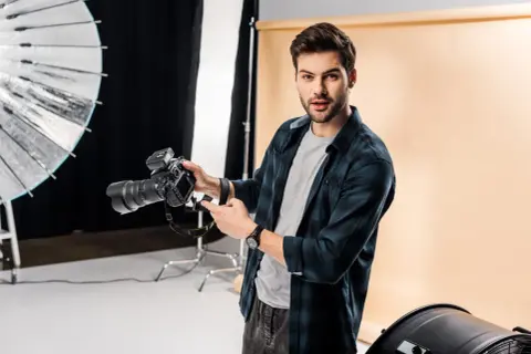 Młody fotograf z aparatem w studio. Chcesz wiedzieć, jak napisać opinie dla fotografa? Oto wskazówki!