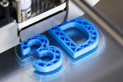 Drukarka 3D tworzy niebieskie litery "3D" z plastiku.
