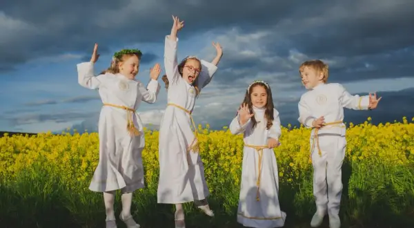 Cztery dzieci w strojach komunijnych skaczą radośnie na tle kwitnącego rzepaku. Zastanawiasz się, ile bierze fotograf za komunie?