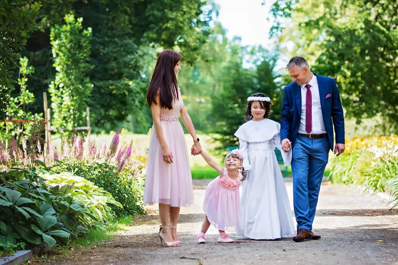 Rodzina spaceruje po parku. Mama w różowej sukience, tata w garniturze, starsza córka w albie, młodsza w różowej sukience. Zastanawiasz się, ile bierze fotograf za komunie?