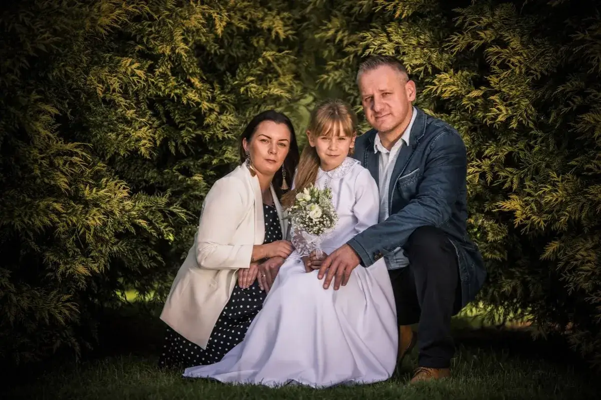Rodzina na tle zieleni. Dziewczynka w bieli trzyma bukiecik. Zastanawiasz się, ile bierze fotograf za komunie?