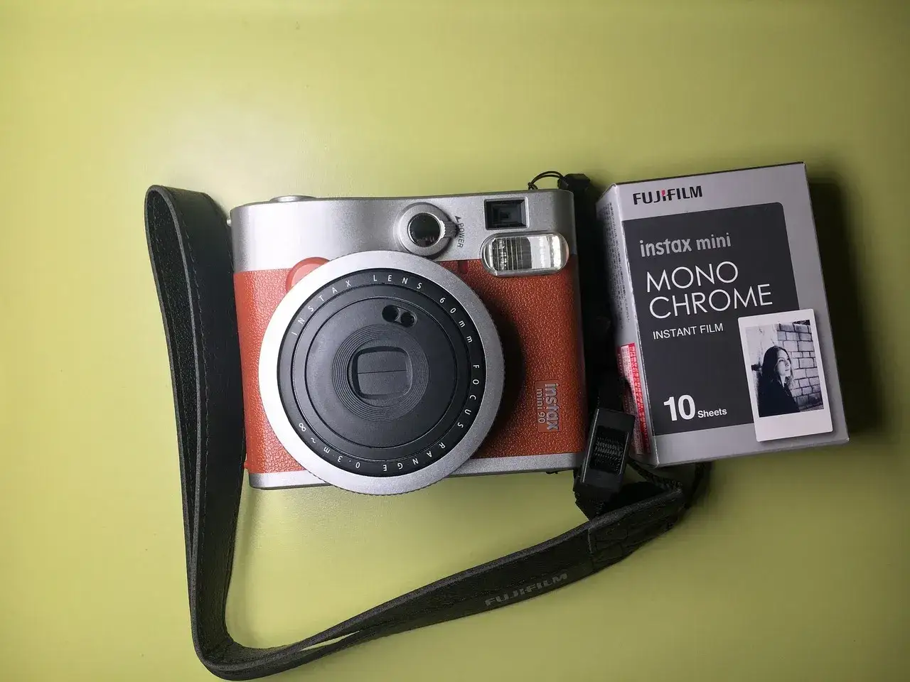Aparat co drukuje zdjęcia, Fujifilm Instax Mini 90, z czarnym paskiem i opakowaniem filmu monochromatycznego.