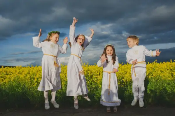 Cztery dzieci w strojach komunijnych skaczą radośnie na tle kwitnącego rzepaku. Zastanawiasz się, ile bierze fotograf za komunie?