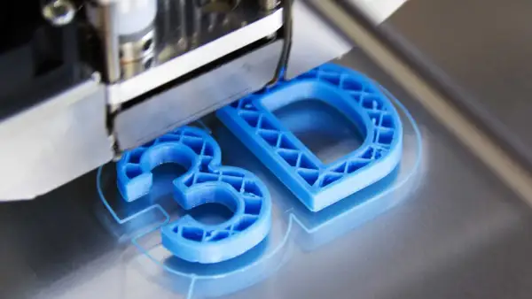 Drukarka 3D tworzy niebieskie litery "3D" z plastiku.